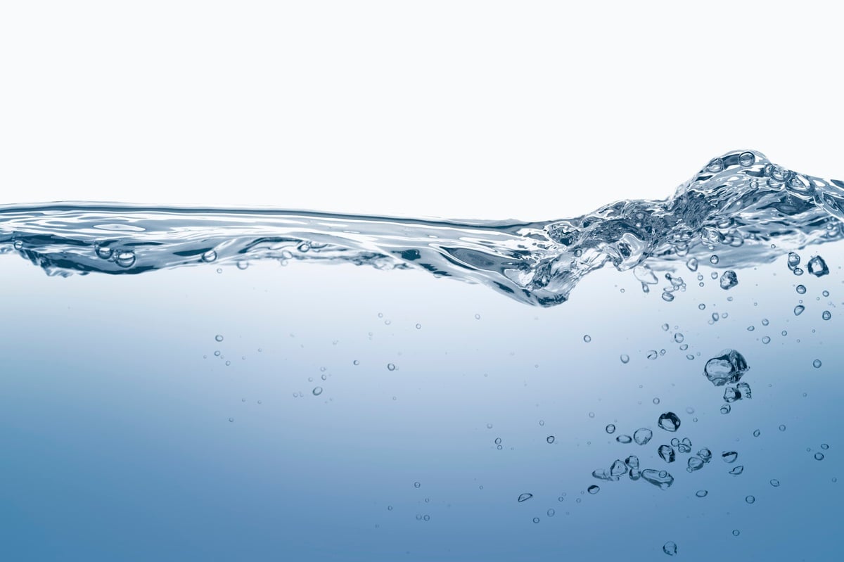 Close-up of clear water with bubbles rising and a splash at the surface, symbolizing purity and movement in water treatment processes.